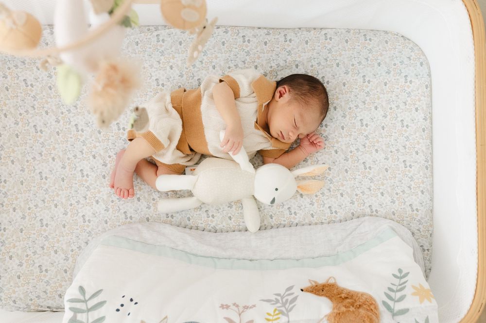 Baby sleeping peacefully on a polka dot mattress with plush toys and floral bedding.