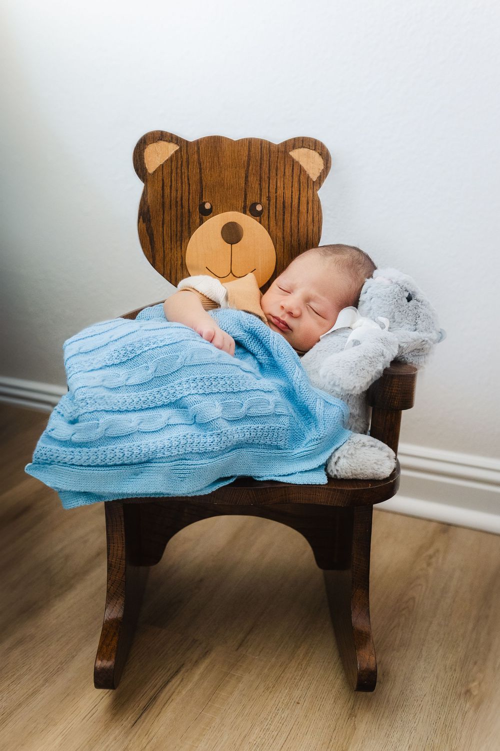 Sleeping newborn on wooden rocking bear bench covered with blue knit blanket.