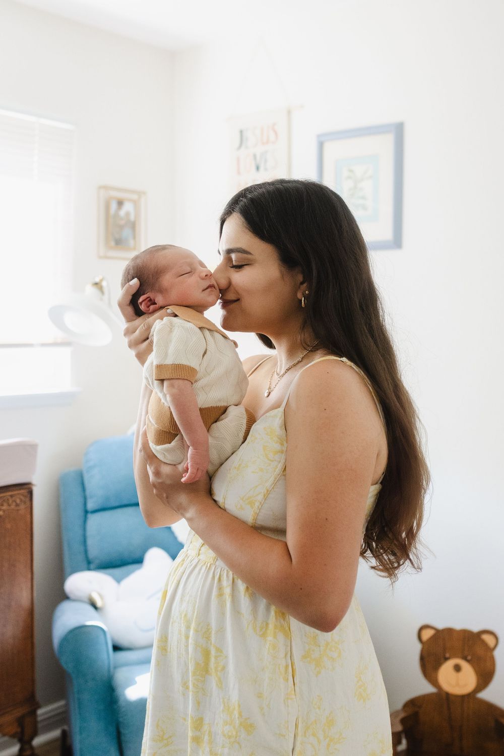A tender moment shared between a parent and baby in a bright living room with blue furniture and framed artwork.