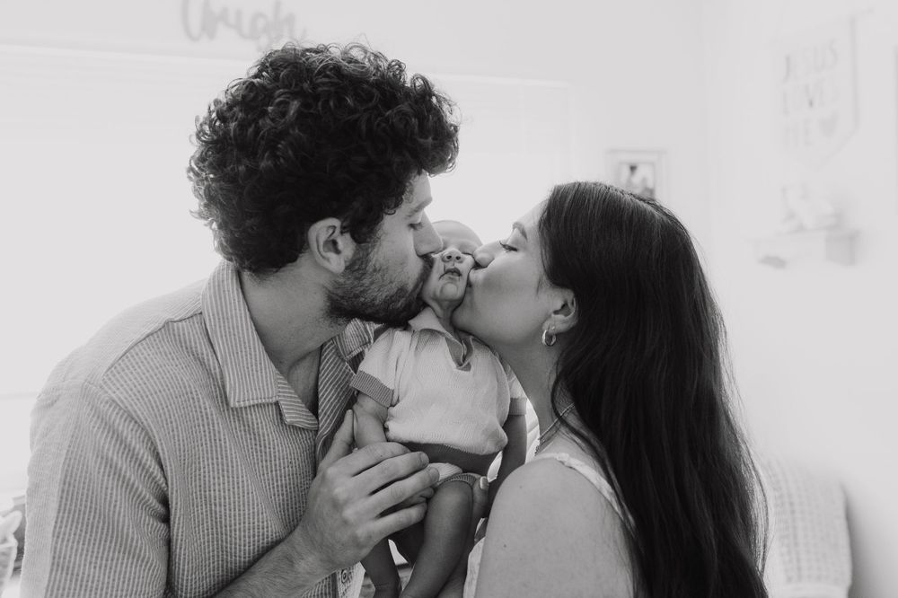 Black and white intimate family moment with parents kissing their baby.