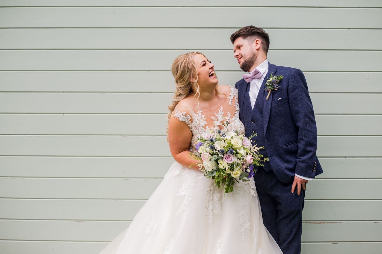 A joyful wedding couple shares a candid moment against a mint green wall.