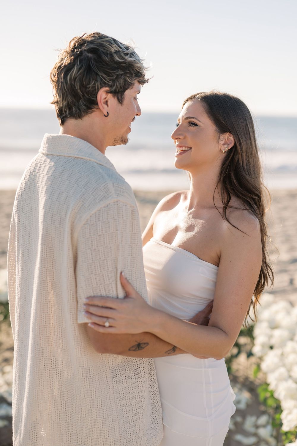 A couple shares an intimate moment on a sunny beach, embracing each other in romantic poses.