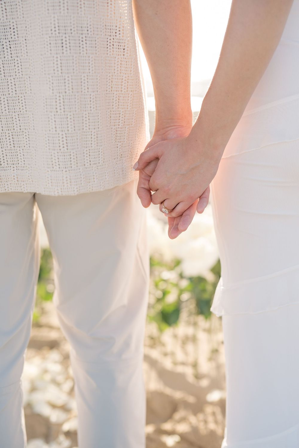 Close-up view of a couple holding hands outdoors, wearing white attire against a soft natural background.