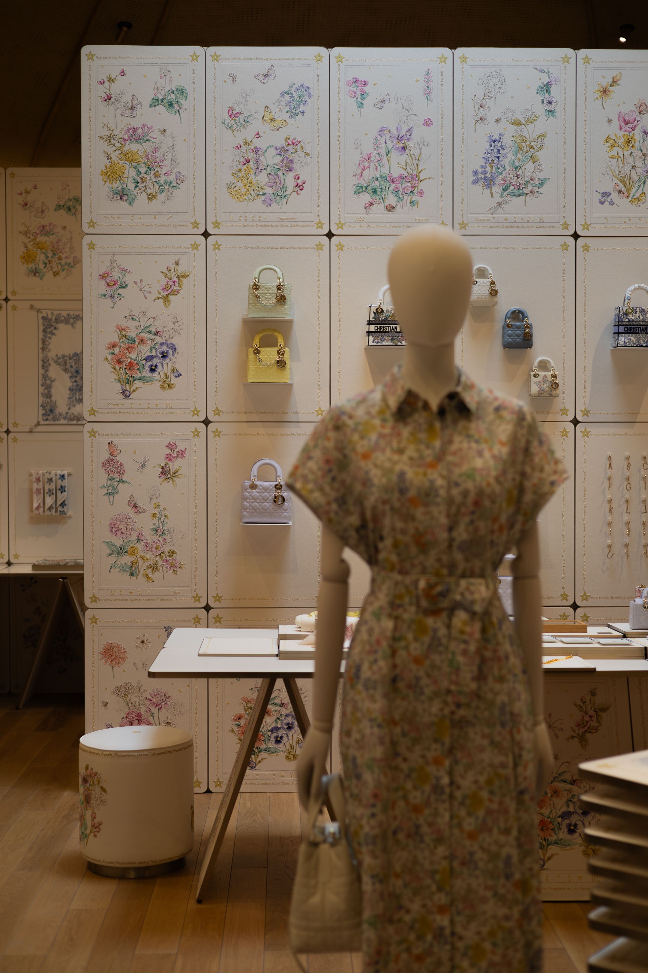 Mannequin wearing floral dress displayed in retail space with botanical artwork and small decorative items on wall.