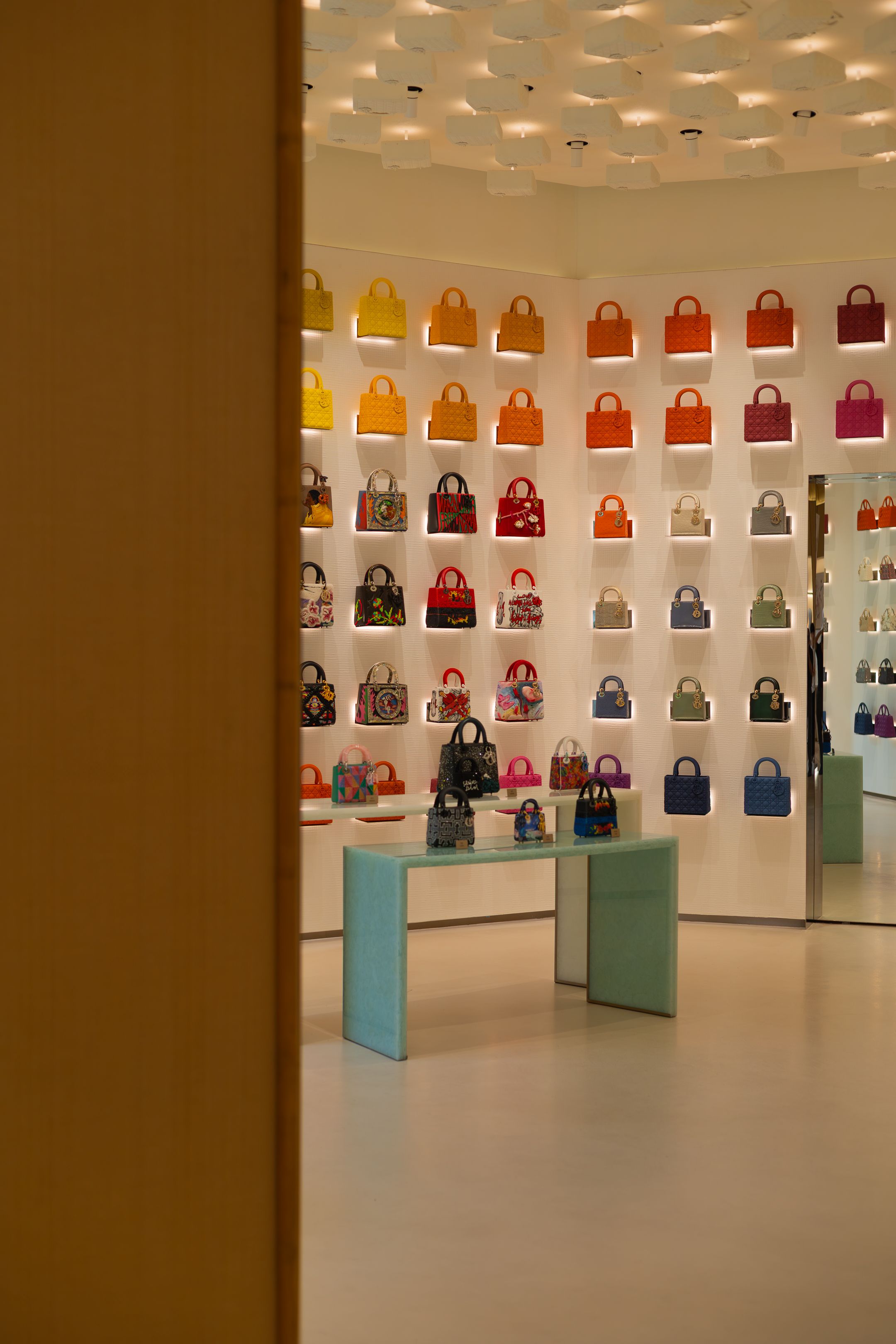 Luxury handbag retail display with colorful purses arranged on white shelves with turquoise display stands in a modern store.