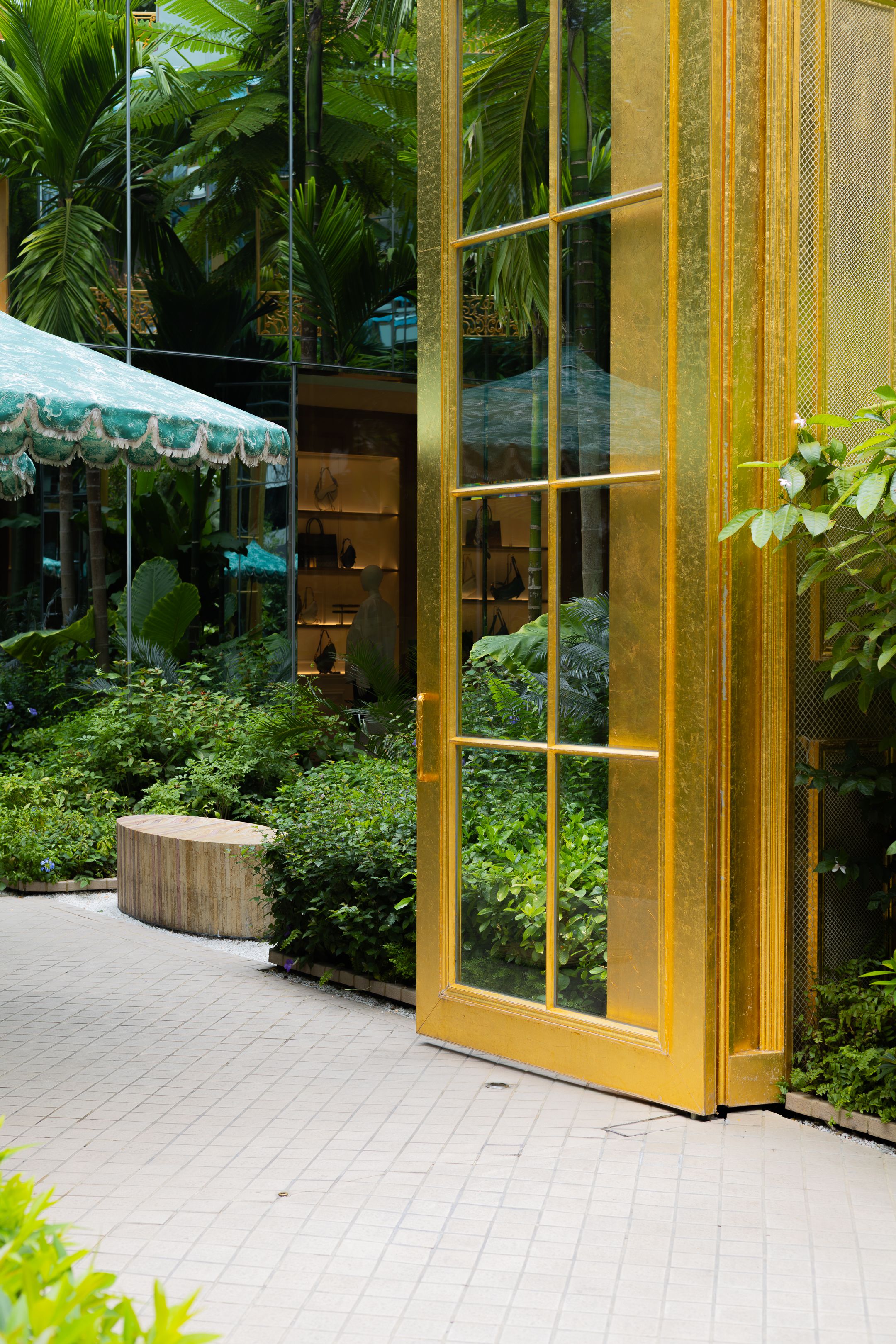 Modern glass and gold building entrance with lush tropical landscaping and white stone pathway.