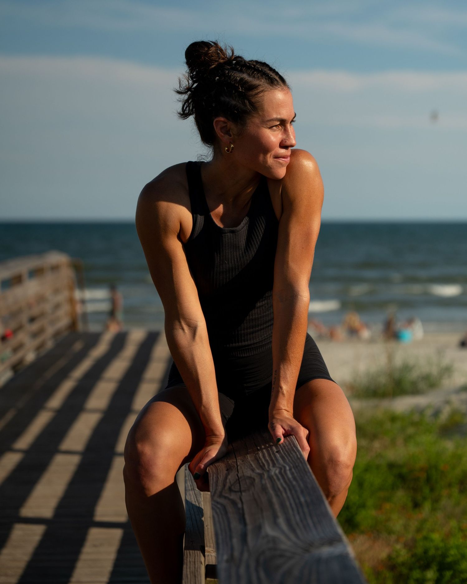 Athletic person stretches and exercises on wooden boardwalk steps near beach during sunset.