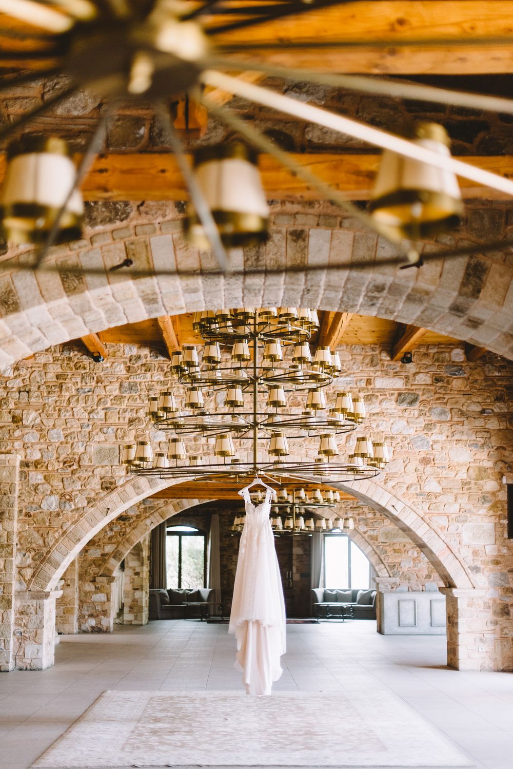 A sequence of white wedding dress photos hanging in an arched stone cellar with exposed wooden beams.