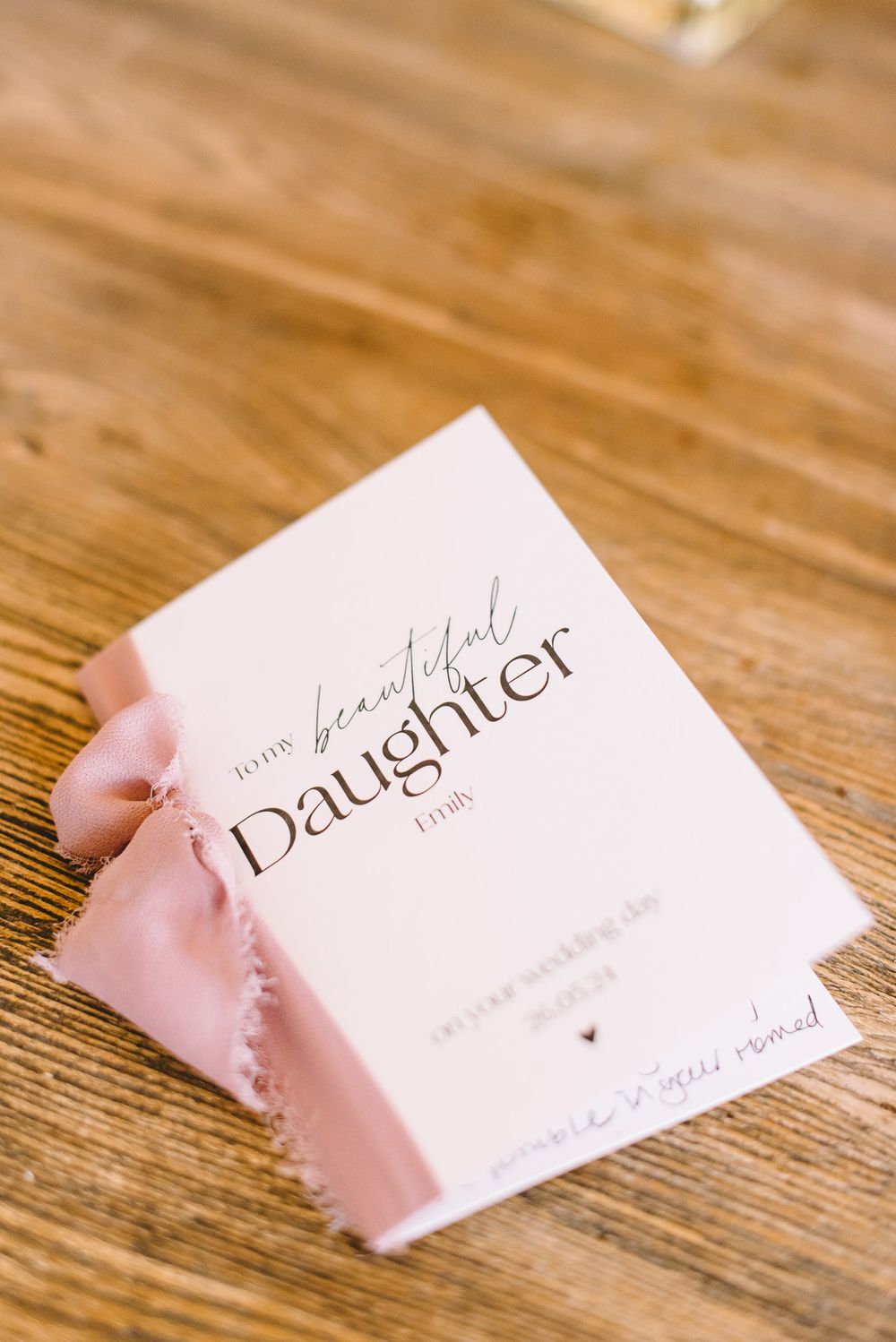 A torn white business card with elegant script text lies on a rustic wooden surface.
