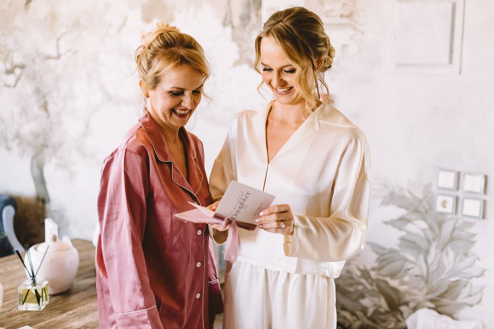 Two people in pink and white outfits share tender moments in a bright, airy room during a photoshoot.