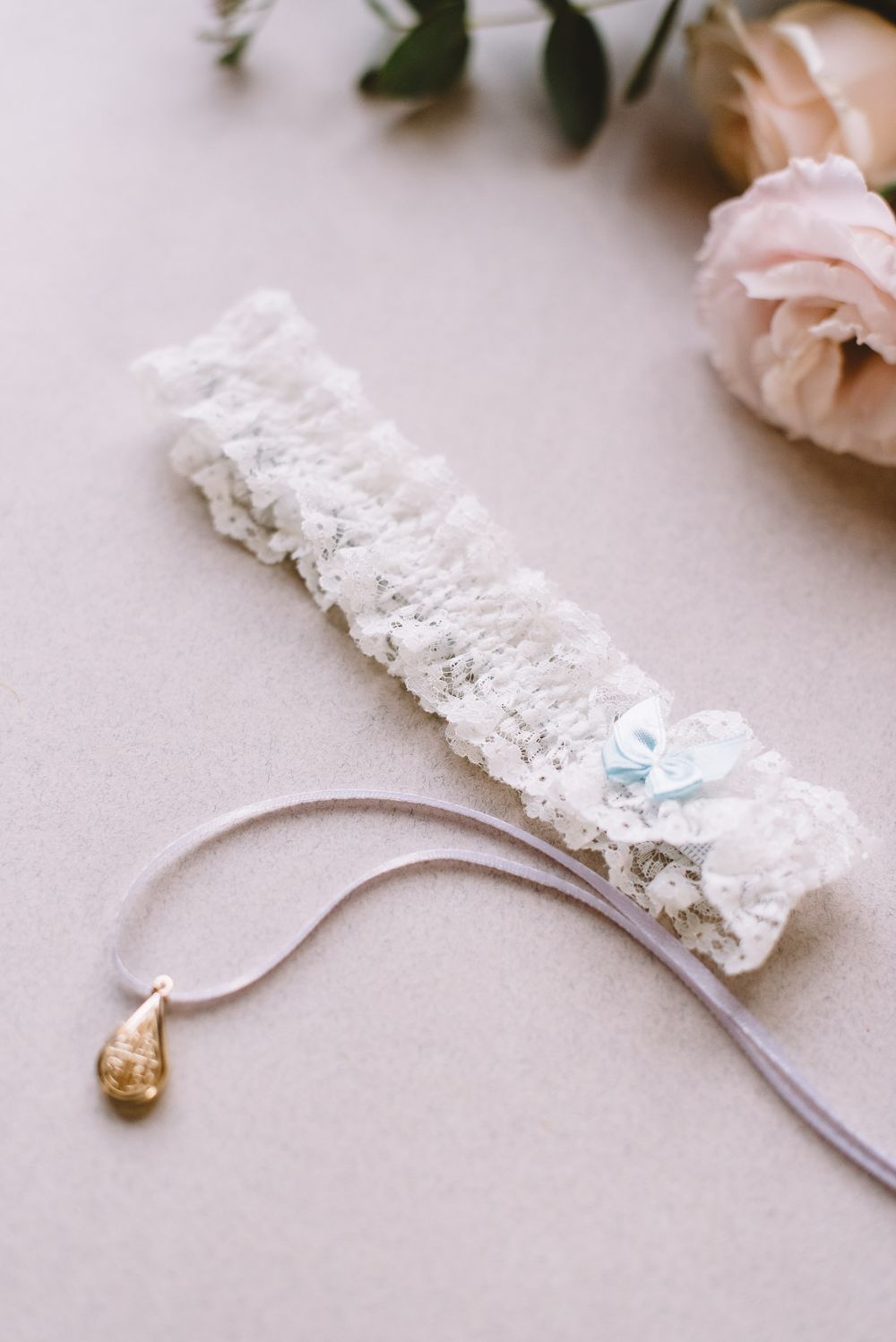 Elegant white lace garter with blue ribbon detail and floral embellishments displayed on a neutral surface.