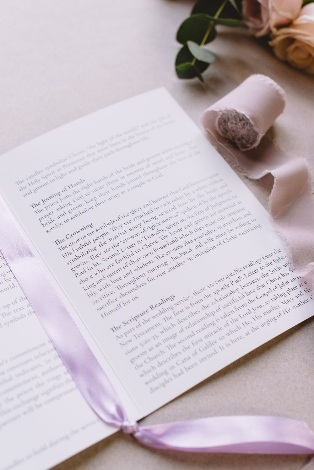 Handwritten letter on white paper with pink ribbon and floral accents in a romantic styled flat lay composition.