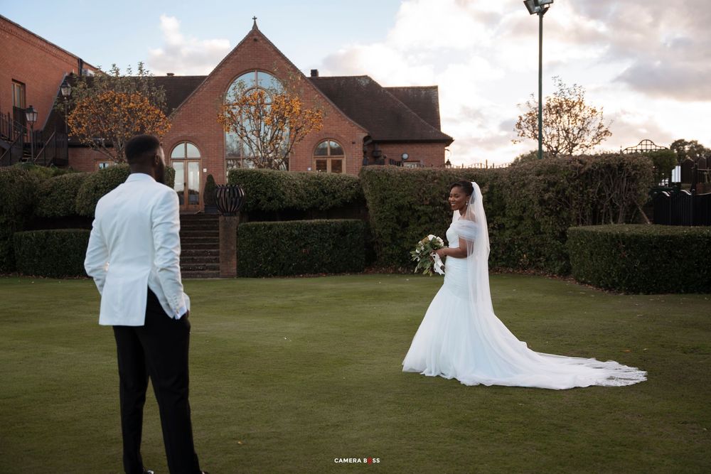 A couple in formal wedding attire poses together on a lush green lawn at sunset.