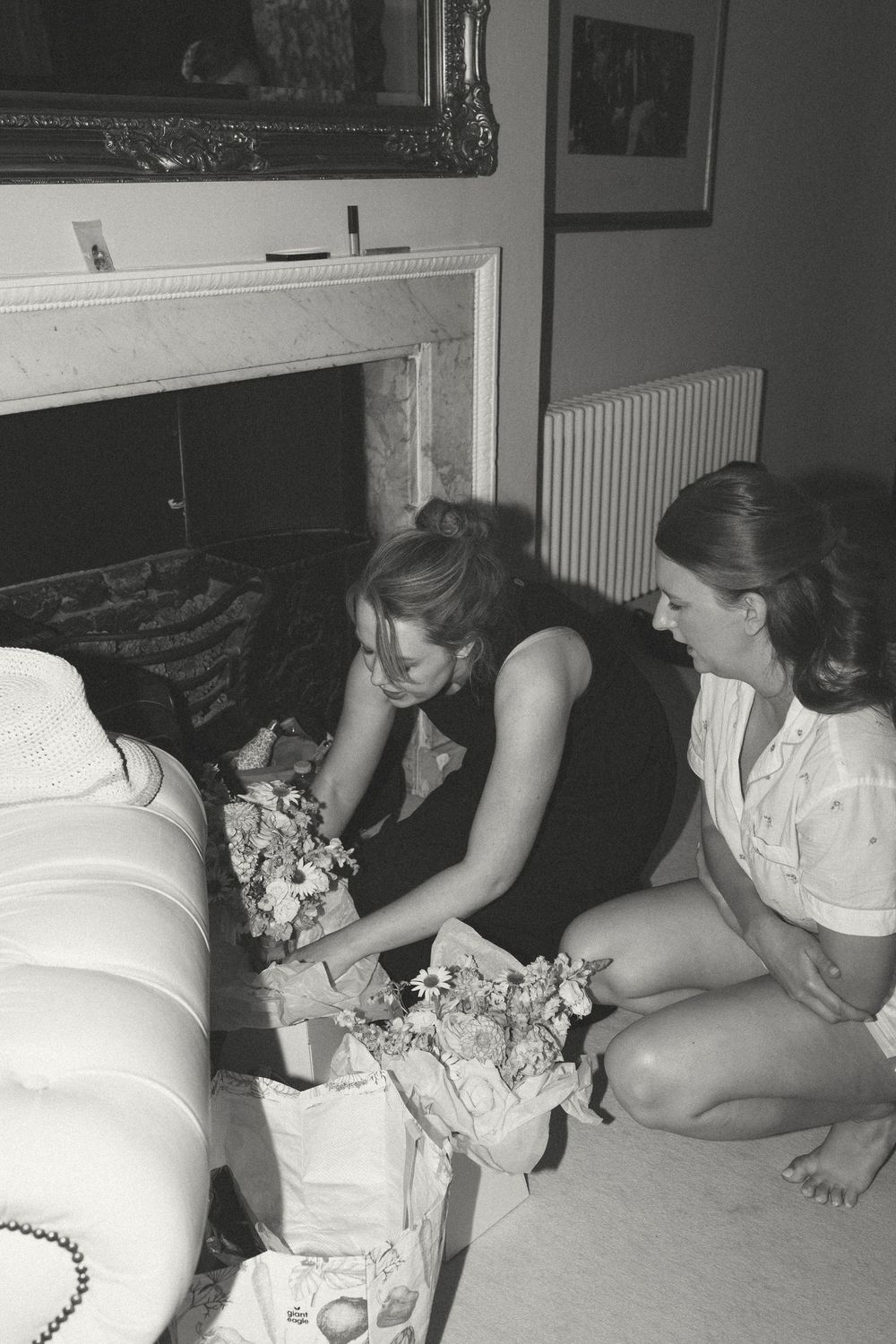 A group gathers around a couch working intently on what appears to be a craft or art project in black and white.