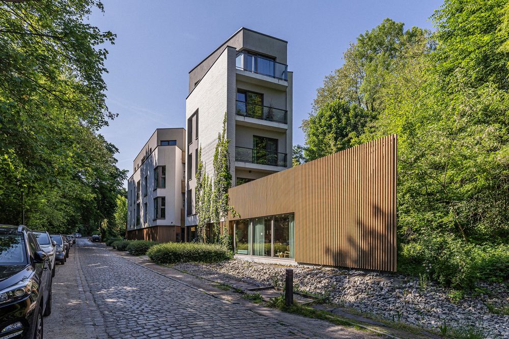 Modern residential buildings with wood accents nestled among trees on a sloping street.