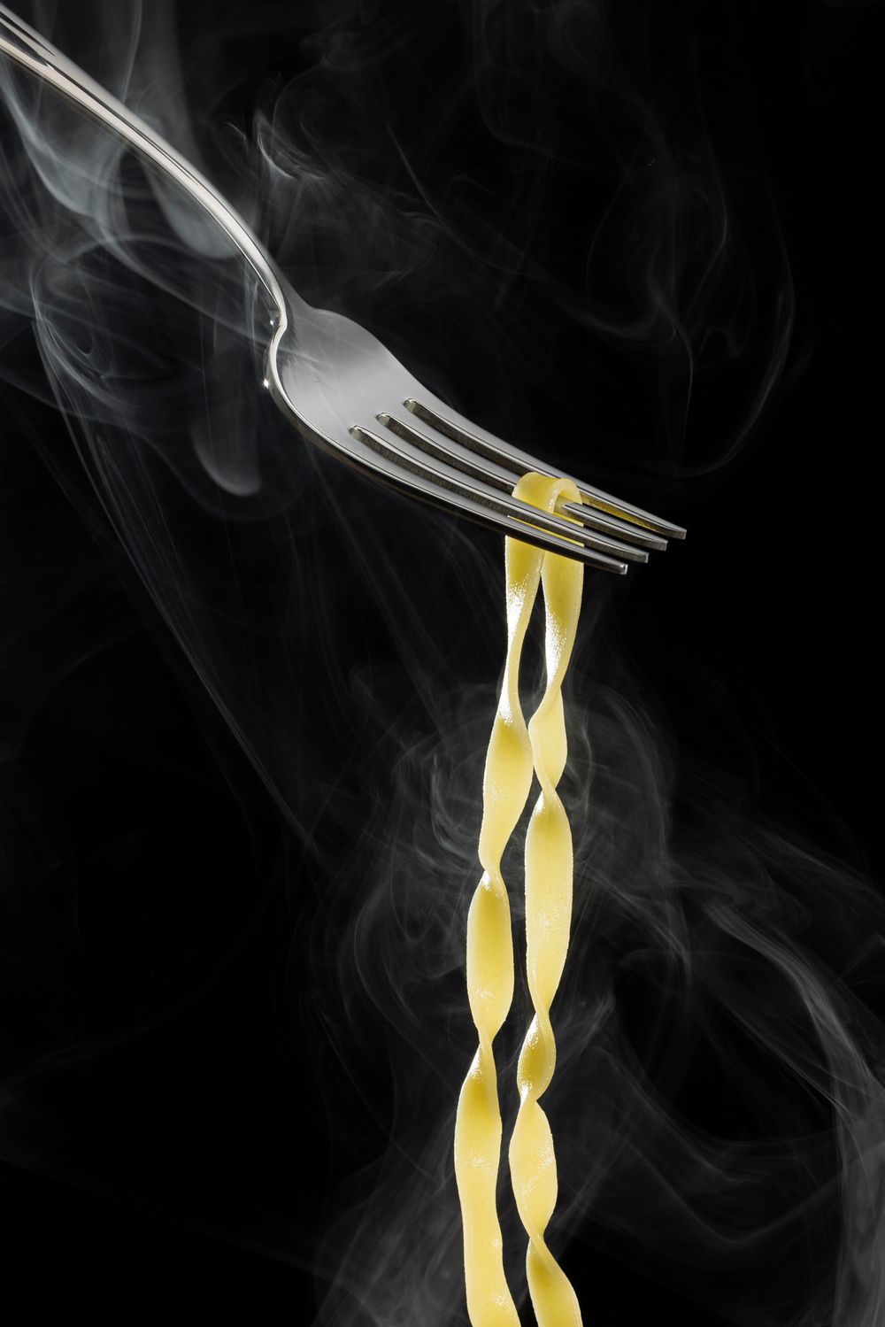 Steam rises around a fork twirling fresh pasta noodles against a black background.