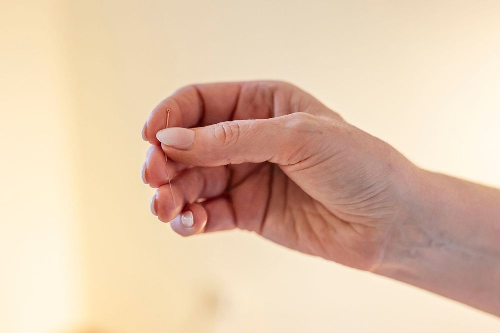 Hands delicately holding or working with small objects against a warm beige background.