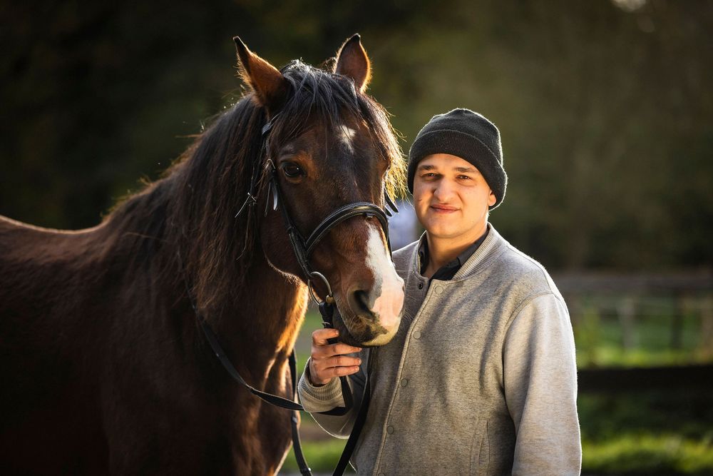 Horse and rider bonding in golden sunlight against a dark natural background.