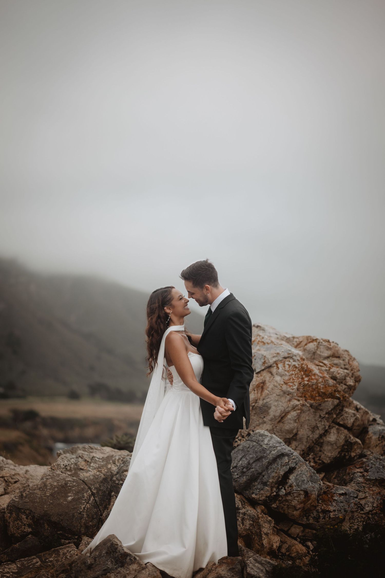 bride and groom smiling and laughing while holding hands slow dancing by the rocks and cliffs