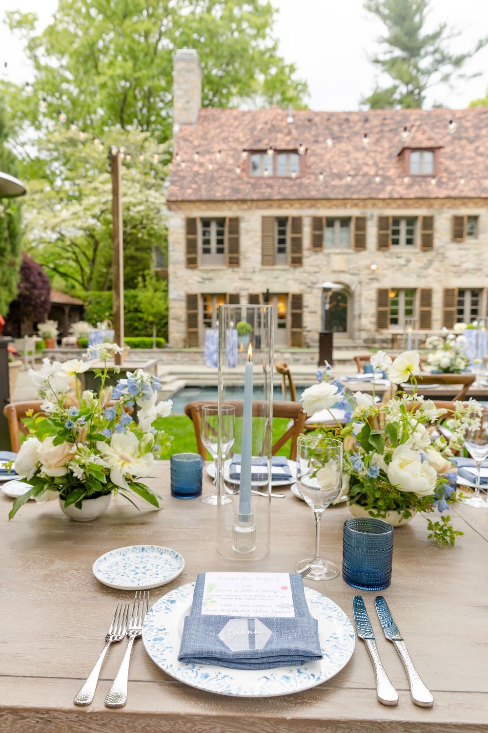 Elegant outdoor table settings with blue and white decor featuring floral centerpieces and crystal glassware at a garden event.