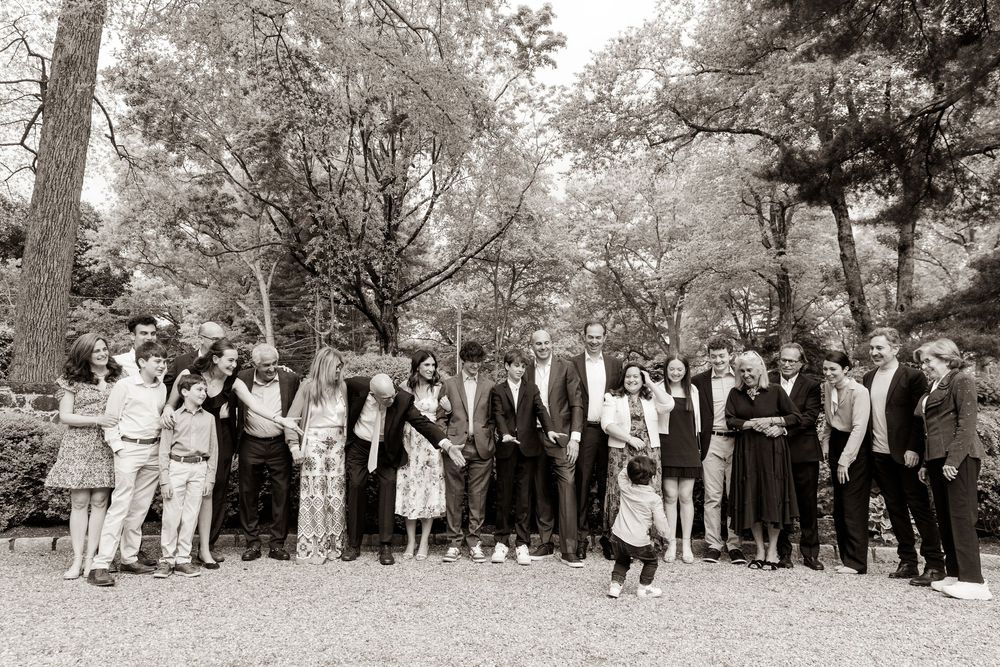 A black and white panoramic photograph showing a large group of people gathered outdoors under trees.