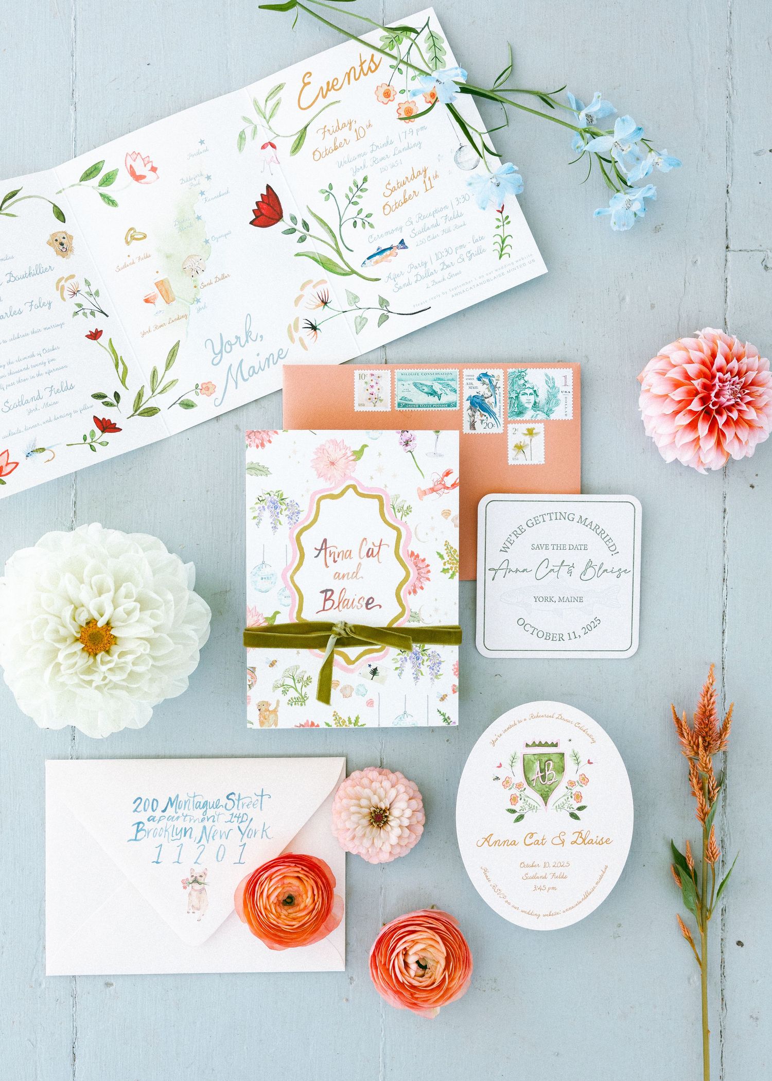 Wedding stationery flat lay with floral designs and coral accents on light blue background.