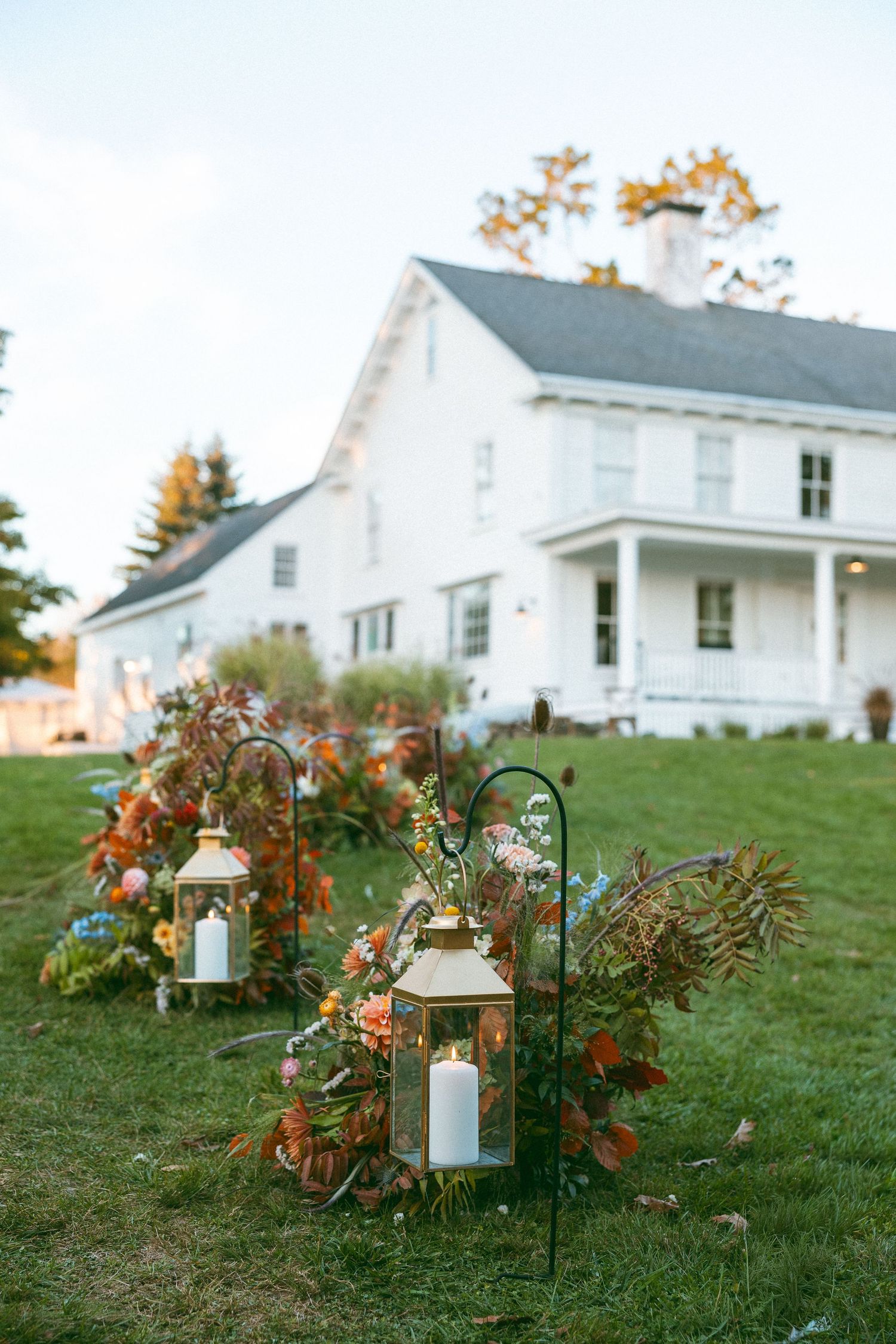 Rustic lanterns and fall decorations line a grassy path leading to white farmhouses.