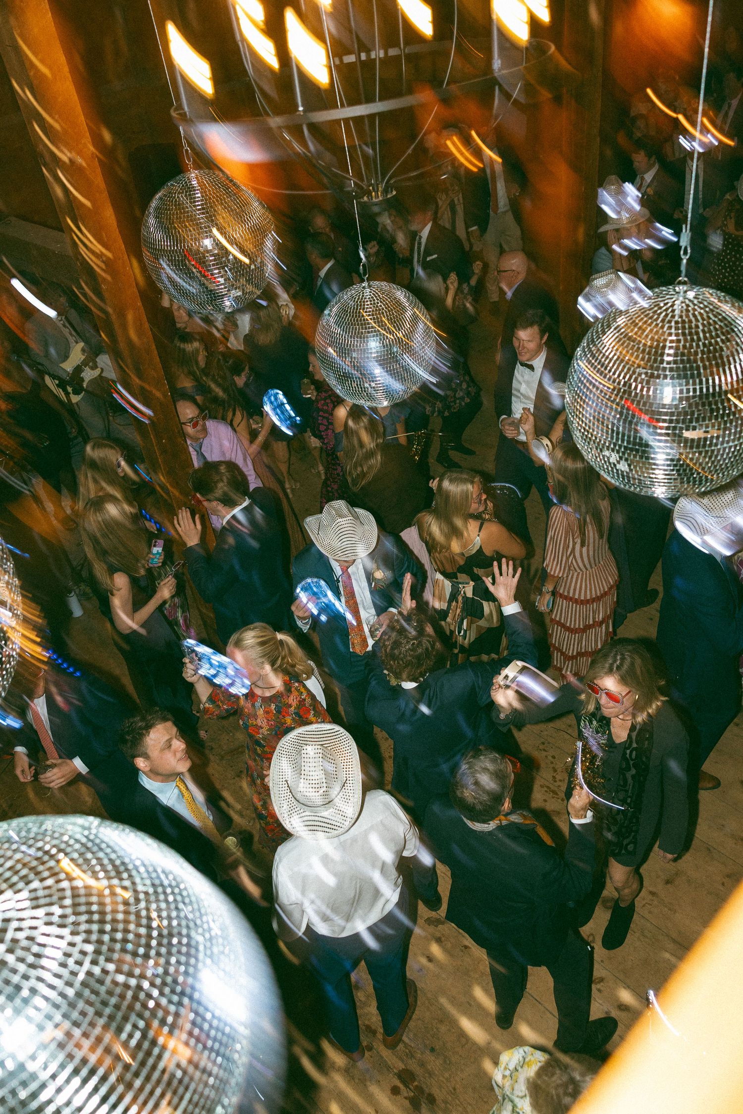 Wedding reception dance party with disco balls and crowd dancing under warm lighting.
