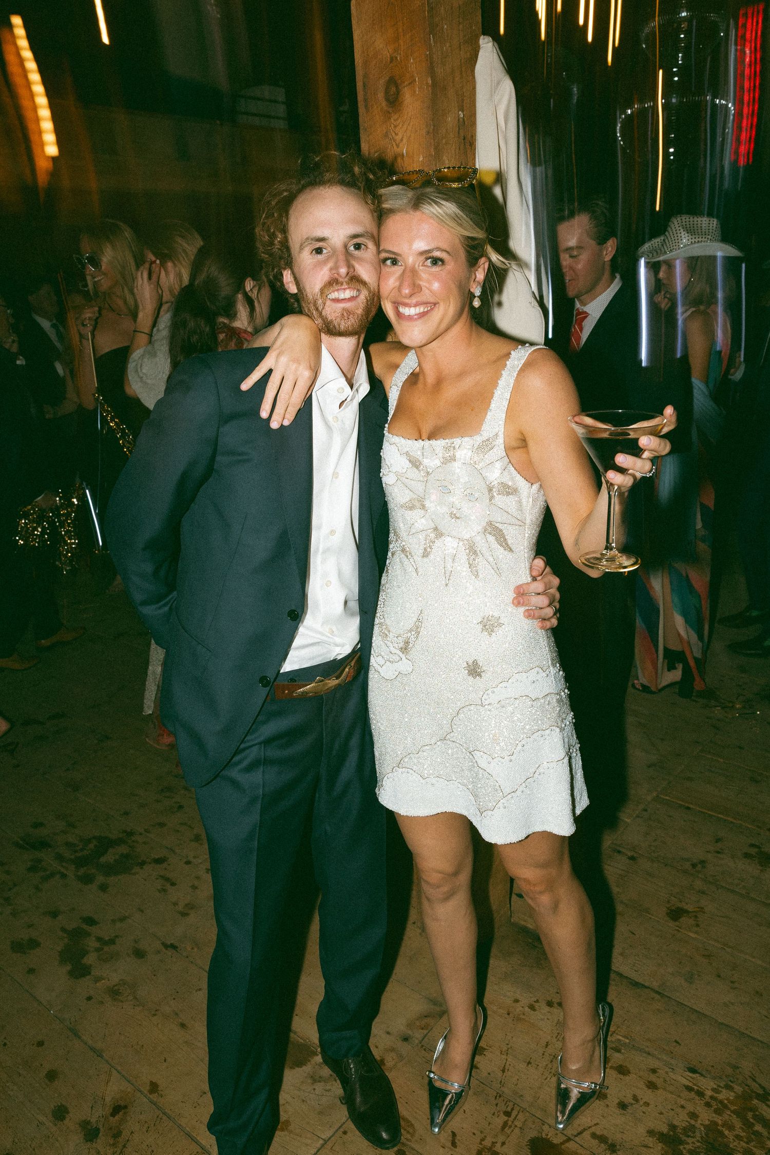Wedding party guests dancing and socializing in a rustic indoor venue.