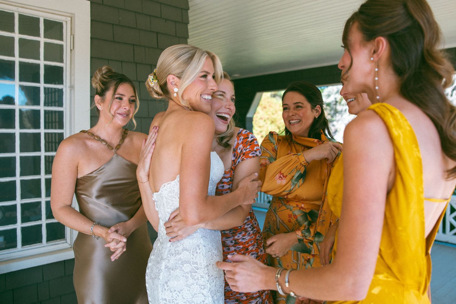 Wedding celebration scene with guests in bright attire gathered on a covered porch.