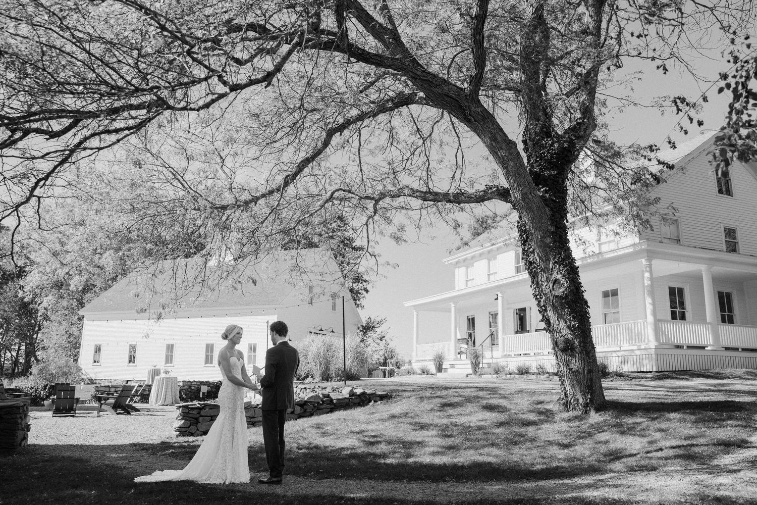 Black and white photograph of a wedding scene with trees and historic buildings in the background.