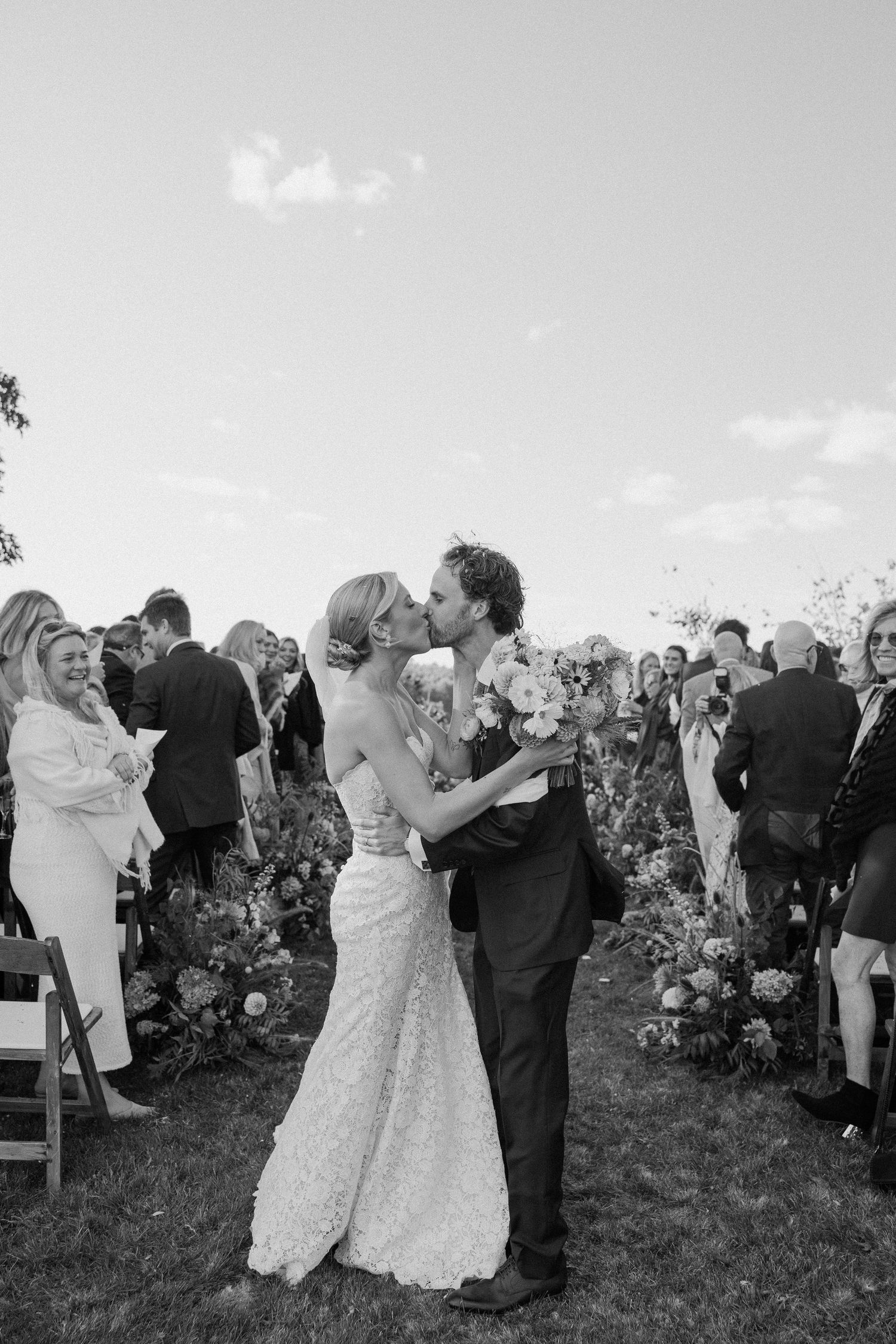 Wedding celebration on a grassy hillside with guests dancing and mingling at sunset.