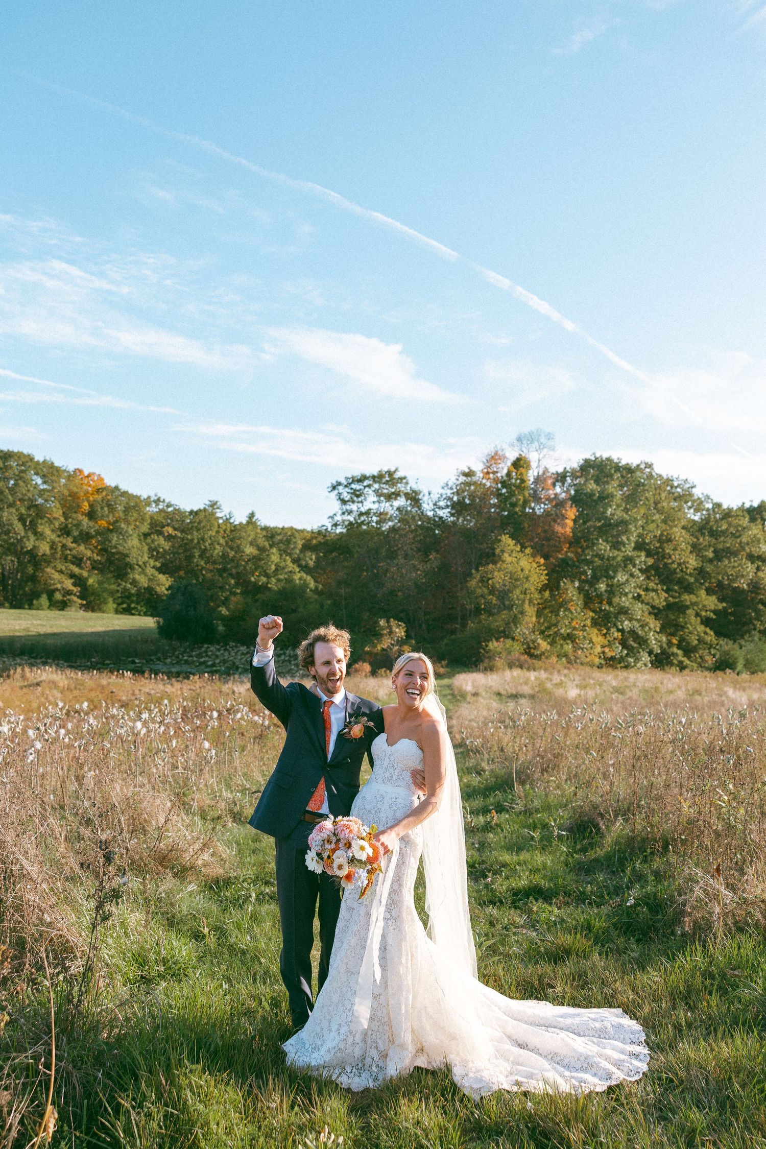 Newlyweds pose for photos in a scenic autumn field under bright blue skies.