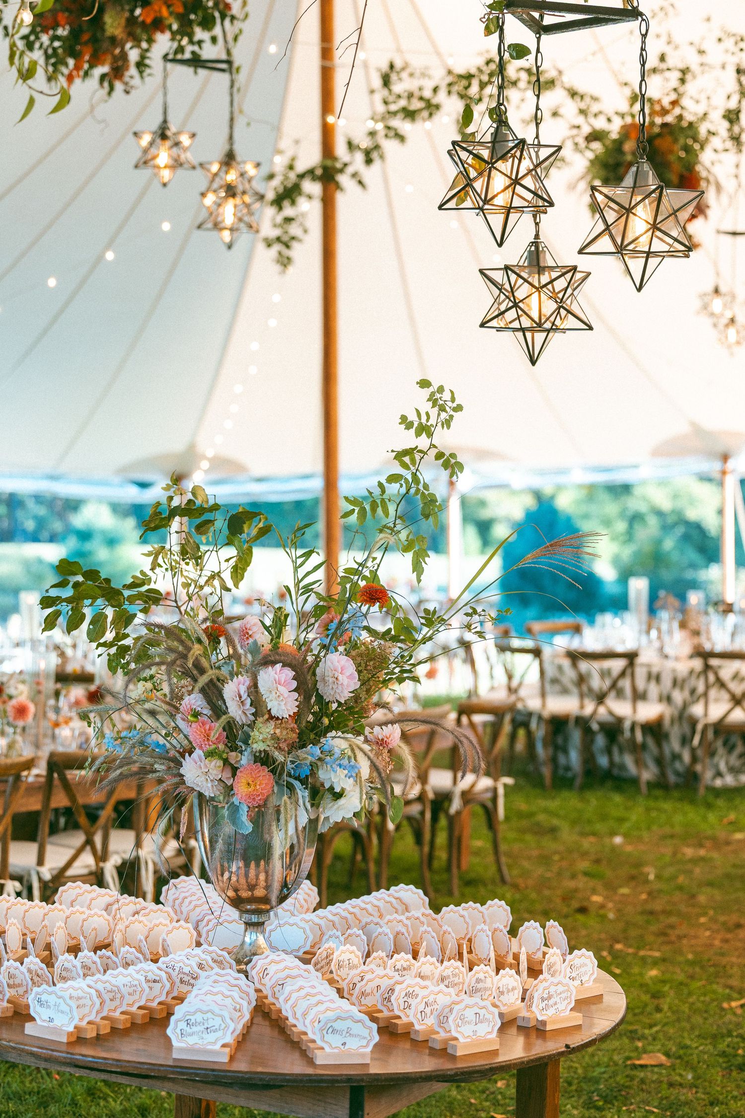 Elegant wedding reception tent decorated with hanging star lanterns and floral arrangements.