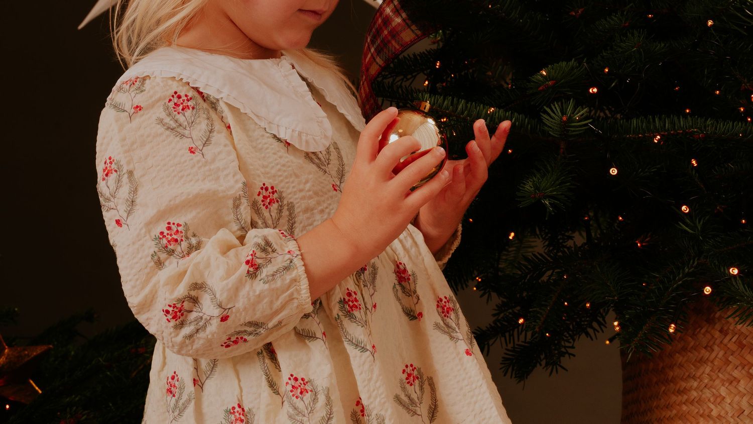 Small decorated Christmas tree in burlap pot against dark background with festive holiday decorations and ornaments.
