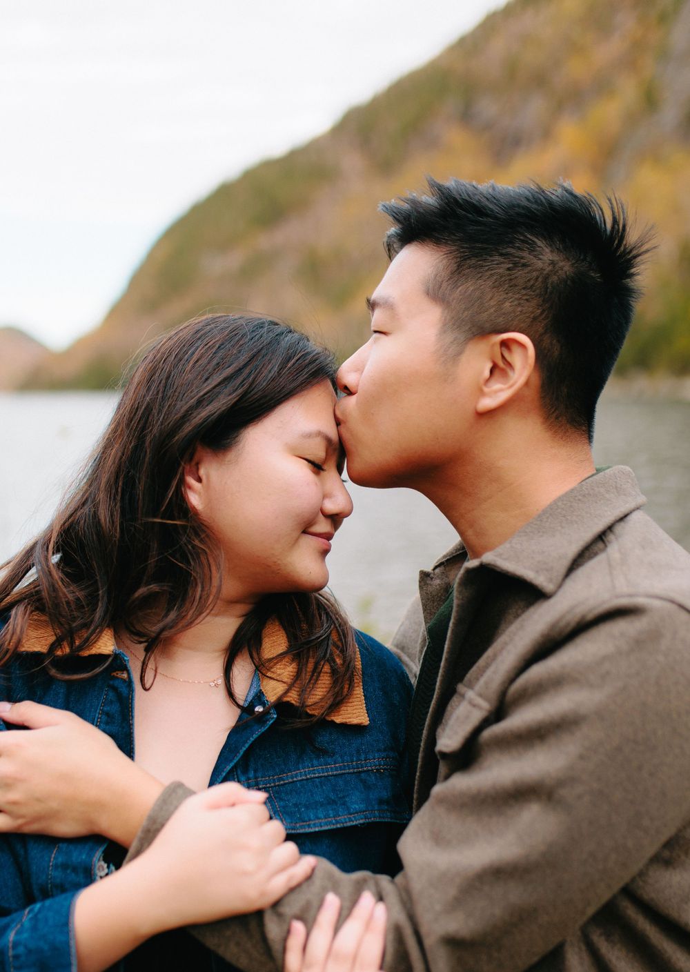 A romantic couple shares an intimate moment on a rocky coastline during golden hour.