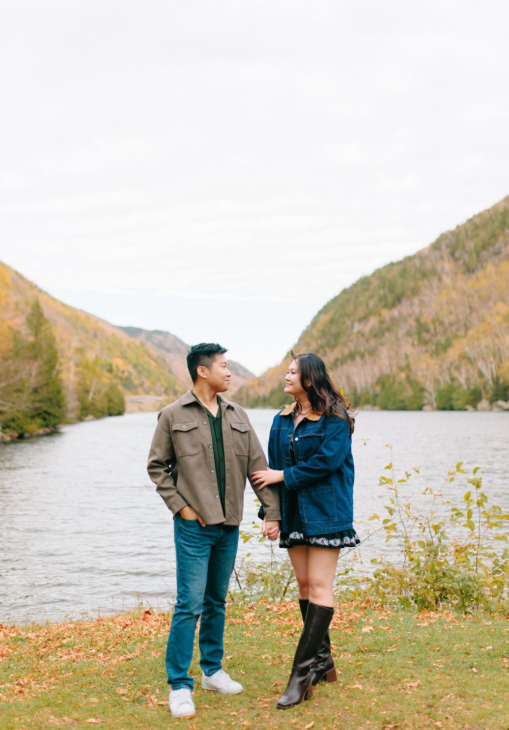 Couple in casual fall attire shares romantic moments by a scenic mountain lake during autumn.