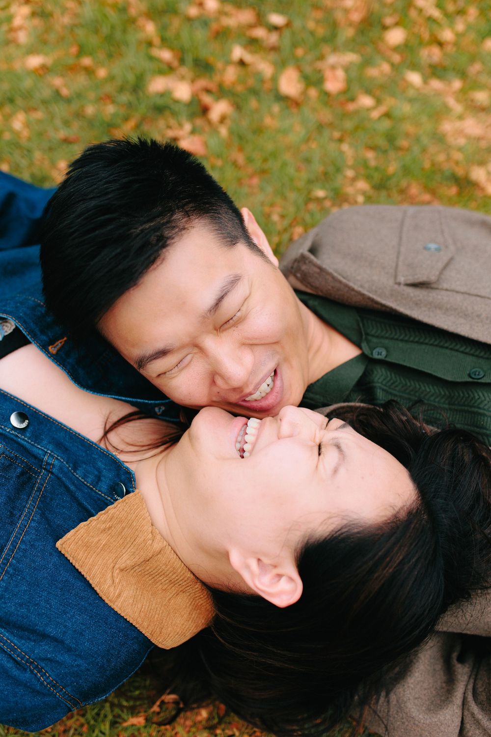 A couple lying on autumn leaves sharing a tender romantic moment in a park setting.
