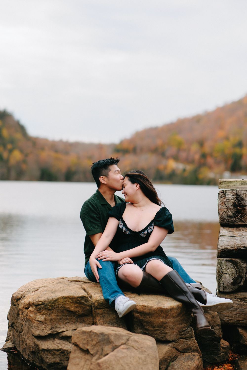 A couple shares romantic moments on rocky lakeside ledges with autumn foliage in the background.