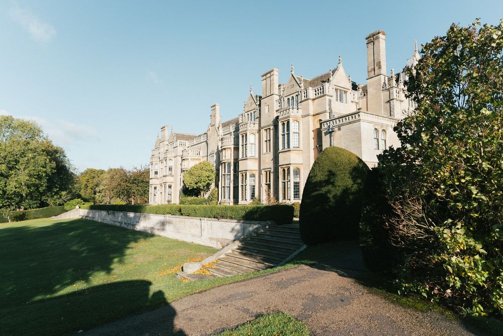 Elegant stone manor house with Gothic architectural features set against a bright sky.