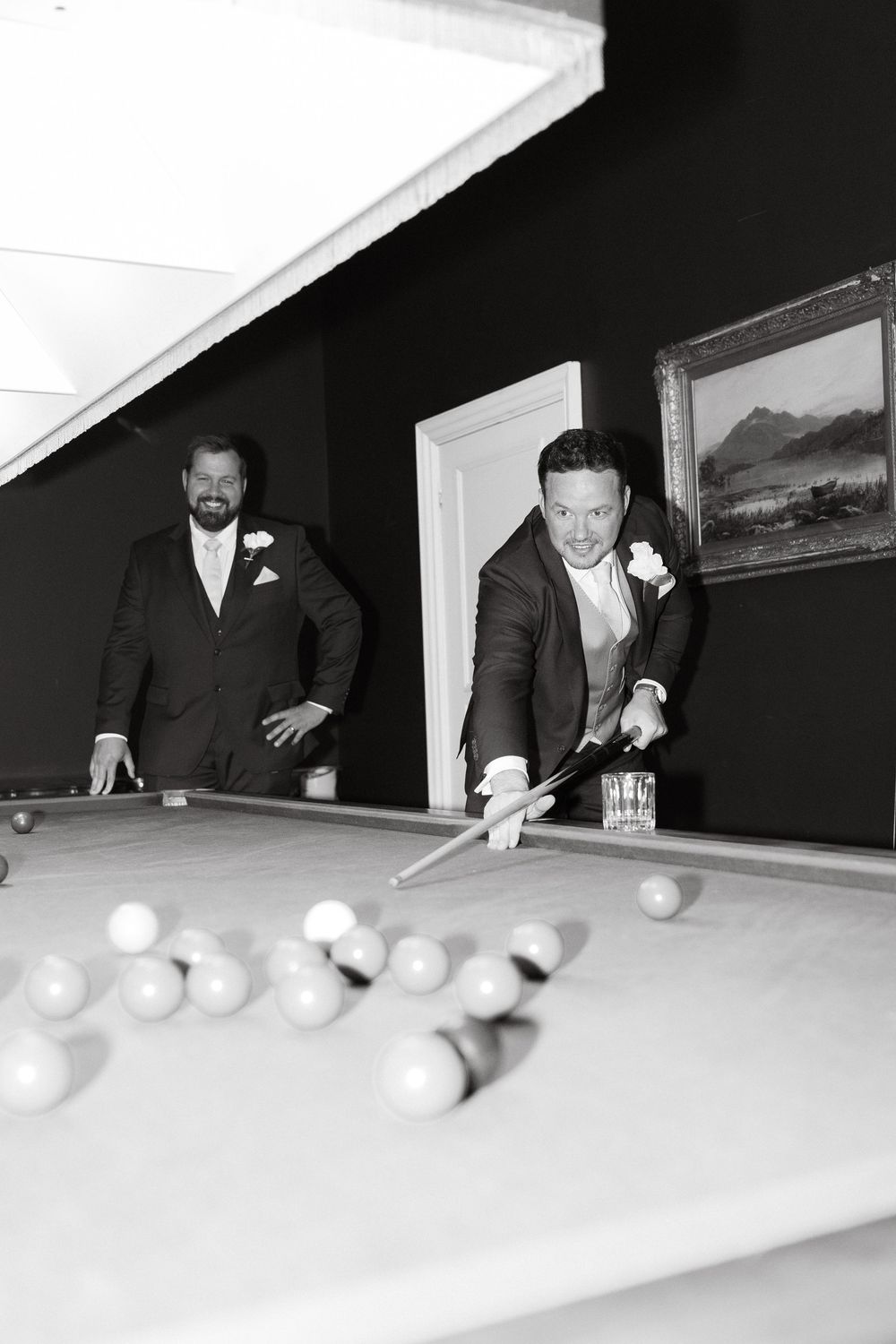 Two people playing pool in formal attire at an elegant venue with a landscape painting on the wall.