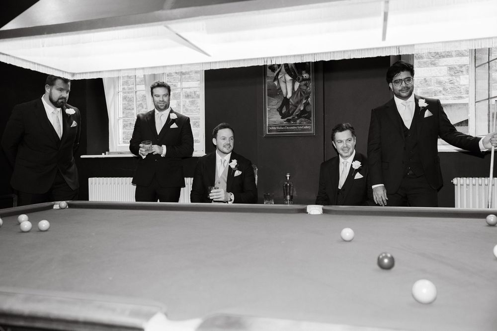 Group gathered around a pool table in formal wear during a wedding celebration.