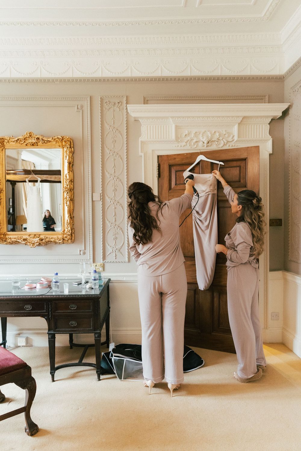 Two people in matching pink pajamas holding up a garment in an elegant dressing room.