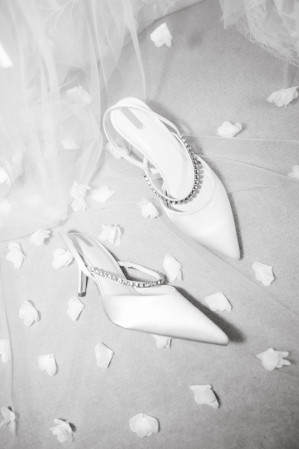 White bridal shoes with decorative details surrounded by scattered flower petals.