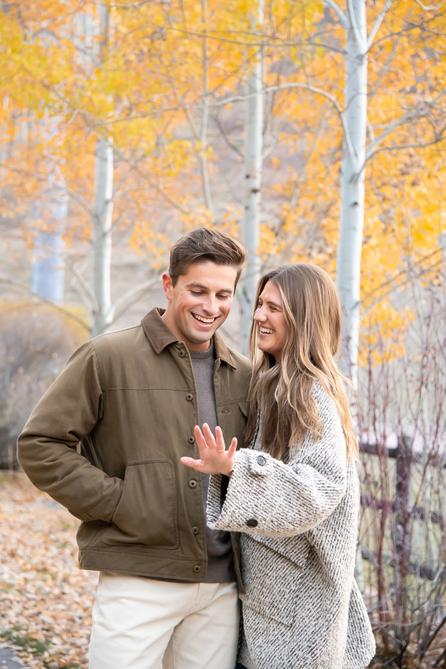 A couple admire the woman's new engagement ring with yellow aspen leaves in the background after a surprise proposal in Vail Village