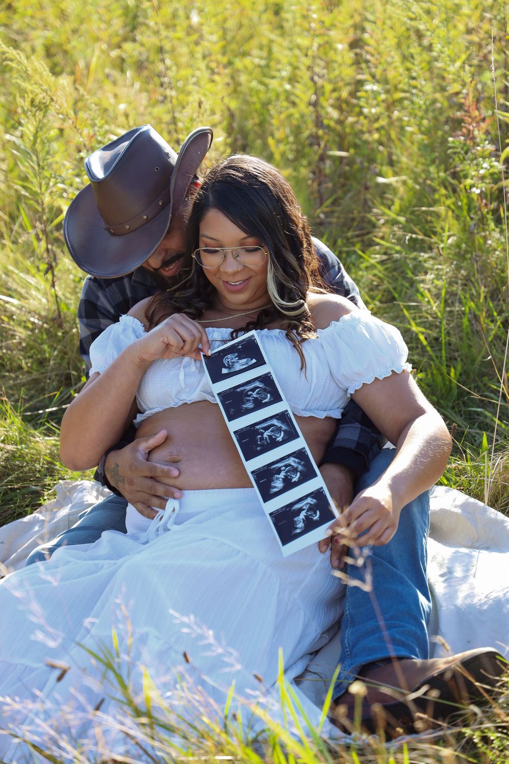 Connecticut maternity photoshoot. Couple sitting in field with ultrasound photos