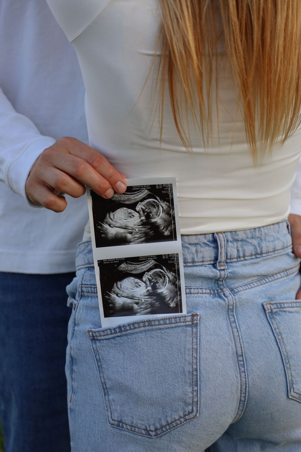 Connecticut maternity photoshoot. Couple standing in field cropped to show ultrasound photos in back jean pocket