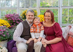 Family portrait in sunlit greenhouse surrounded by yellow and purple mums.