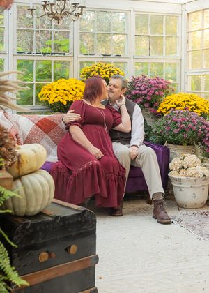 Greenhouse setting with fall decorations featuring mums, pumpkins and rustic bench.