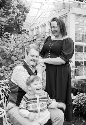 Black and white family portrait in greenhouse setting with natural lighting.